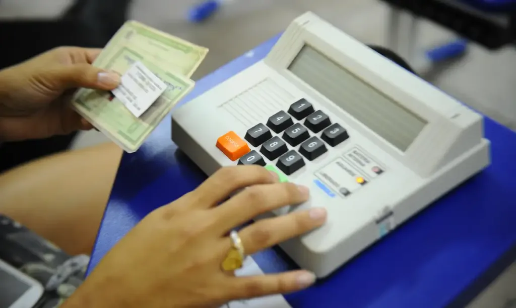 Pessoa com documentos do eleitor digitando liberação na urna eletrônica