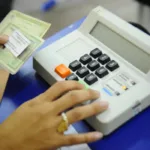 Pessoa com documentos do eleitor digitando liberação na urna eletrônica