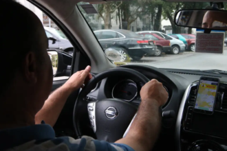 Motorista dirige por avenida olhando aplicativo de corrida. Foto: Rovena Rosa/Agência Brasil