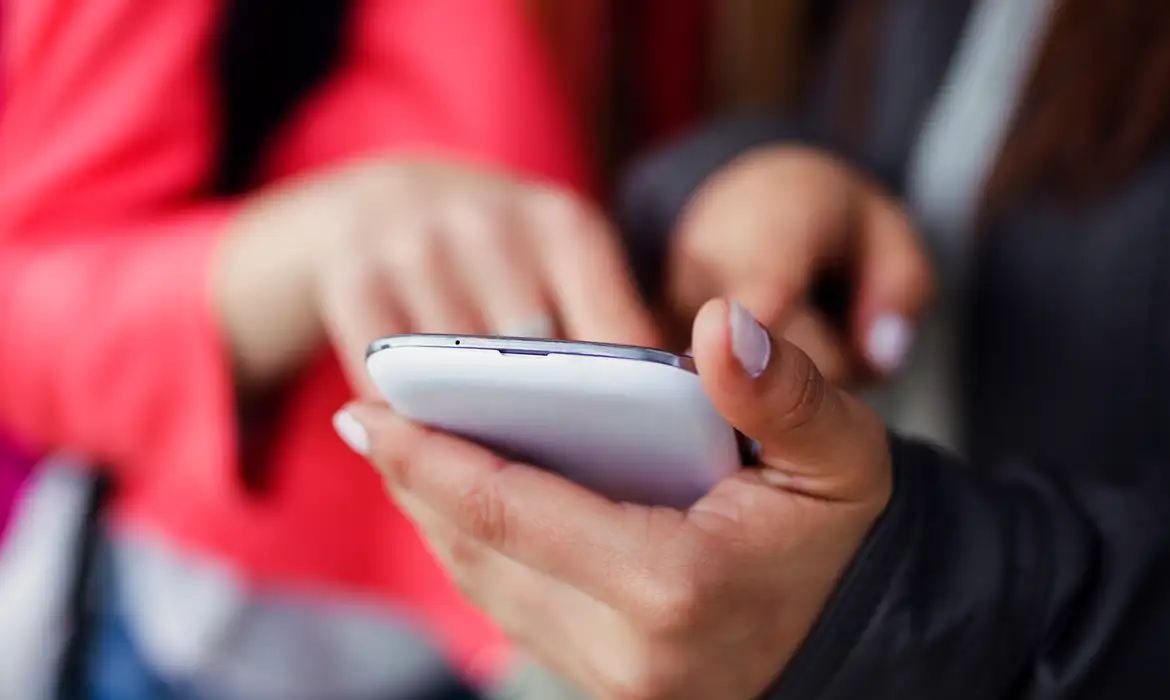 two-beautiful-students-using-mobile-phone-street_rede_social